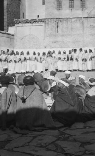 Large troupe of Berber Women and musicians performing in a courtyard. The foreground is in focus but the dance troupe further away from the camera is out of focus.Telouet, 13th January 1936.