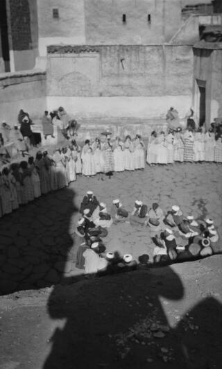 Berber Women Dancers and male musicians (seated) performing in a courtyard. The photographers shadow can be seen in the foreground. Telouet, 13th January 1936.