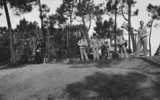 David and Gwilym Lloyd George on a golf course in Portugal. Gwilym is standing on the tee with a club in his hand, David is sitting on a bench looking the other way.