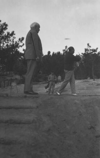 David Lloyd George (on the left of the picture) watches as Gwilym drives off from a tee, Estoril, Portugal. Two caddies are watching from a distance.