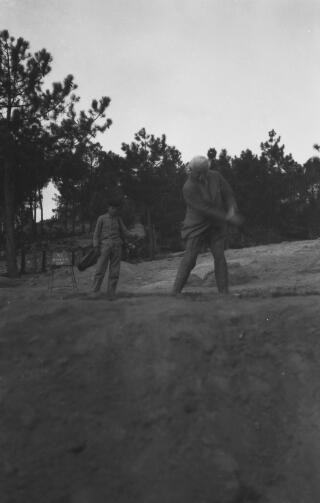 David Lloyd George driving off from a tee, watched by a caddy.