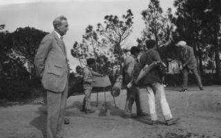 David Lloyd George teeing off, watched by three caddies and a middle aged man. Estoril, Portugal.