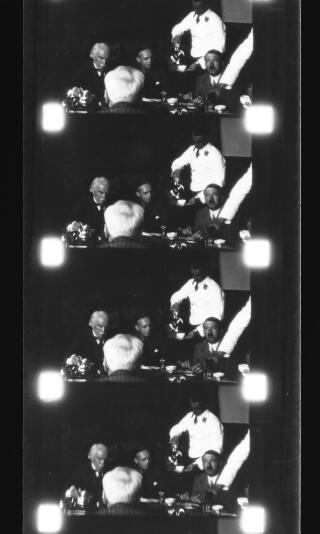 A copy of four frames from a cinefilm showing Adolf Hitler and David Lloyd George drinking coffee. A waiter is pouring Hitler's coffee. Von Ribbentrop is seated between, but slightly behind, them. The back of Thomas Jones head can be seen in the foreground.