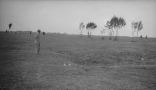 Gwilym Lloyd George standing in a field looking at a small depression, presumed to be connected to his WW1 military service.
