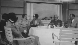 L-R Megan Lloyd George, Mrs Sylvester, Margaret, Edna, David and Gwilym Lloyd George sitting at a dining table on a hotel terrace. A coffee pot and cups are on the table.