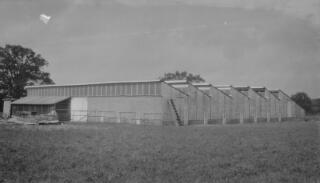A large building in a field designed to let in a lot of daylight. Building appears brand new. Location and purpose not known.