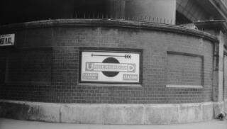 Sign on a brick wall pointing to Charing Cross Underground Station with an arrow pointing to the left.