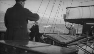 David Lloyd George (in greatcoat and white peaked cap) and Margaret (in fur coat) negotiate their way along the deck of 'Sabrina.' A rough sea is running and the coastline visible in the distance.