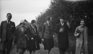 Three women and two men walking along a track, a hedge behind them on the right.