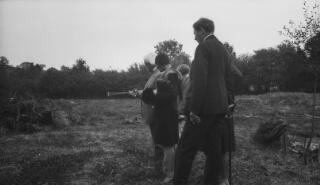 D Ll G and others standing in a field and looking at something out of the frame of the photo. Lloyd George has a small impliment in his hand.