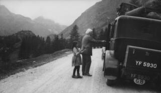 Lloyd George is about to enter a car parked on the side of the road in an alpine setting. A young girl appears to be offering him a bunch of flowers. This may be the incident referred to by Sylvester on p185 of 'The Real Lloyd George' "...while enjoying a picnic tea peasant children presented us with bunches of Edelweiss. L.G. was thrilled and insisted on speaking to the children and giving each a present of money."