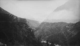 A steep hillside on which is an isolated farm approached via a track. At the base of the hillside is a stream. Location unknown.