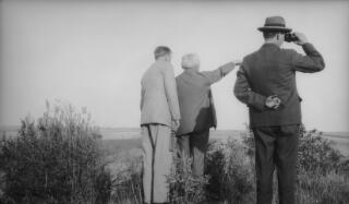 David Lloyd George pointing at the horizon in the company of Gwilym Lloyd George and Inspector Pavey. Pavey is looking through binoculars. All have their backs to the camera.