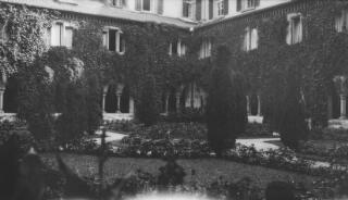 Formal gardens in front of a large building, possibly a hotel. The ground floor appears to be cloistered.