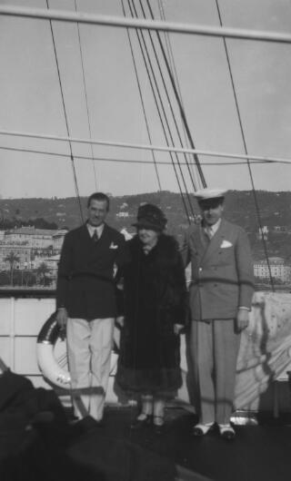 A slightly out of focus group photo, the sitters on the deck of 'Sabrina' the coastline visible behind them.The yacht appears to be anchored at Santa Margherita Ligure.