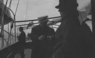 Lloyd George being handed a pair of binoculars by a person standing near the camera and therefore out of focus.