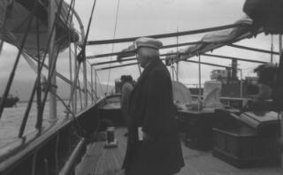 David Lloyd George in peaked cap and greatcoat looking out to sea from the deck of the 'Sabrina.'