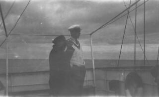 Gwilym Lloyd George (in white cricketing sweater) in conversation with the ships captain. The captain is looking through binoculars.