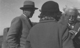 Gwilym and Megan (with back to camera) look on as David Lloyd George looks through a book.