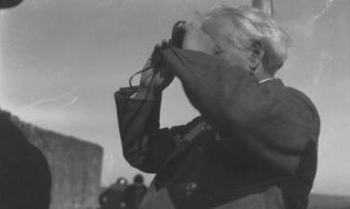 David Lloyd George looking through a pair of binoculars, facing left.