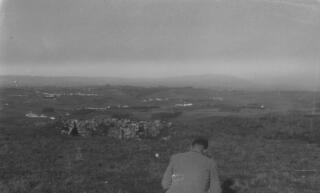 Gwilym Lloyd George with his back to the camera in an unknown rural location. There appears to be a stone structure in the middle distance, possibly the remains of one of the dugouts visited by G Ll G on the 1930 European Tour.