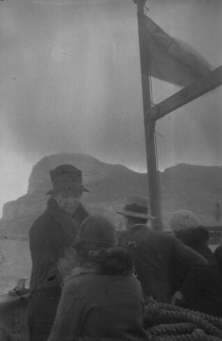 A man and three women aboard a British registered vessel with a rocky coastline behind them.